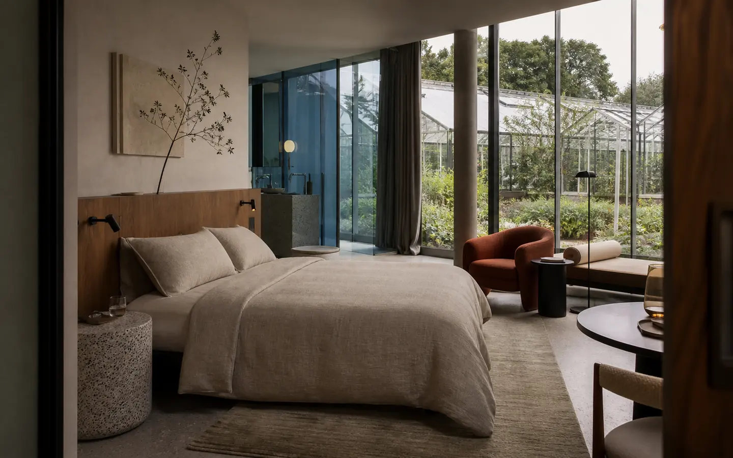 Suite met linnen bed, paprika fauteuil en uitzicht op een kas
